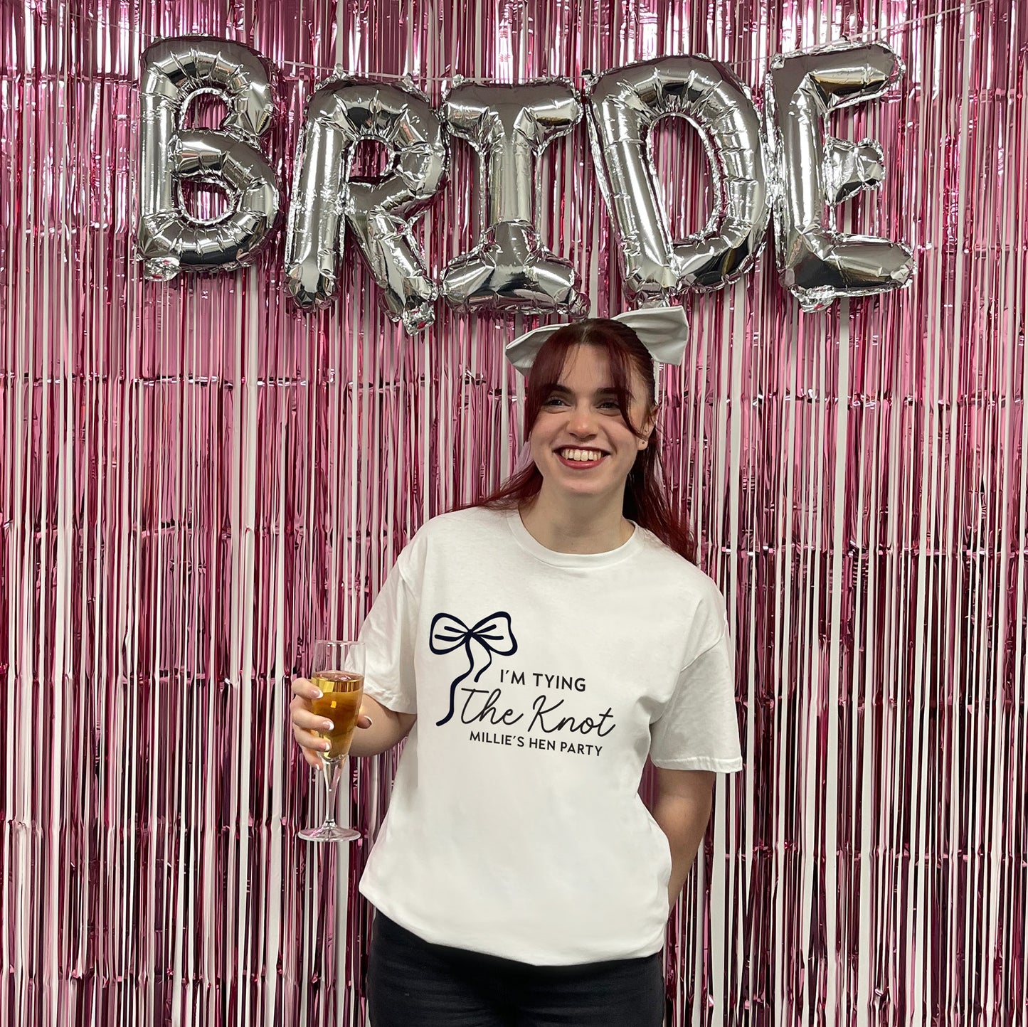 Woman holding a glass of champagne with 'Bride' balloons and pink tinsel in the background