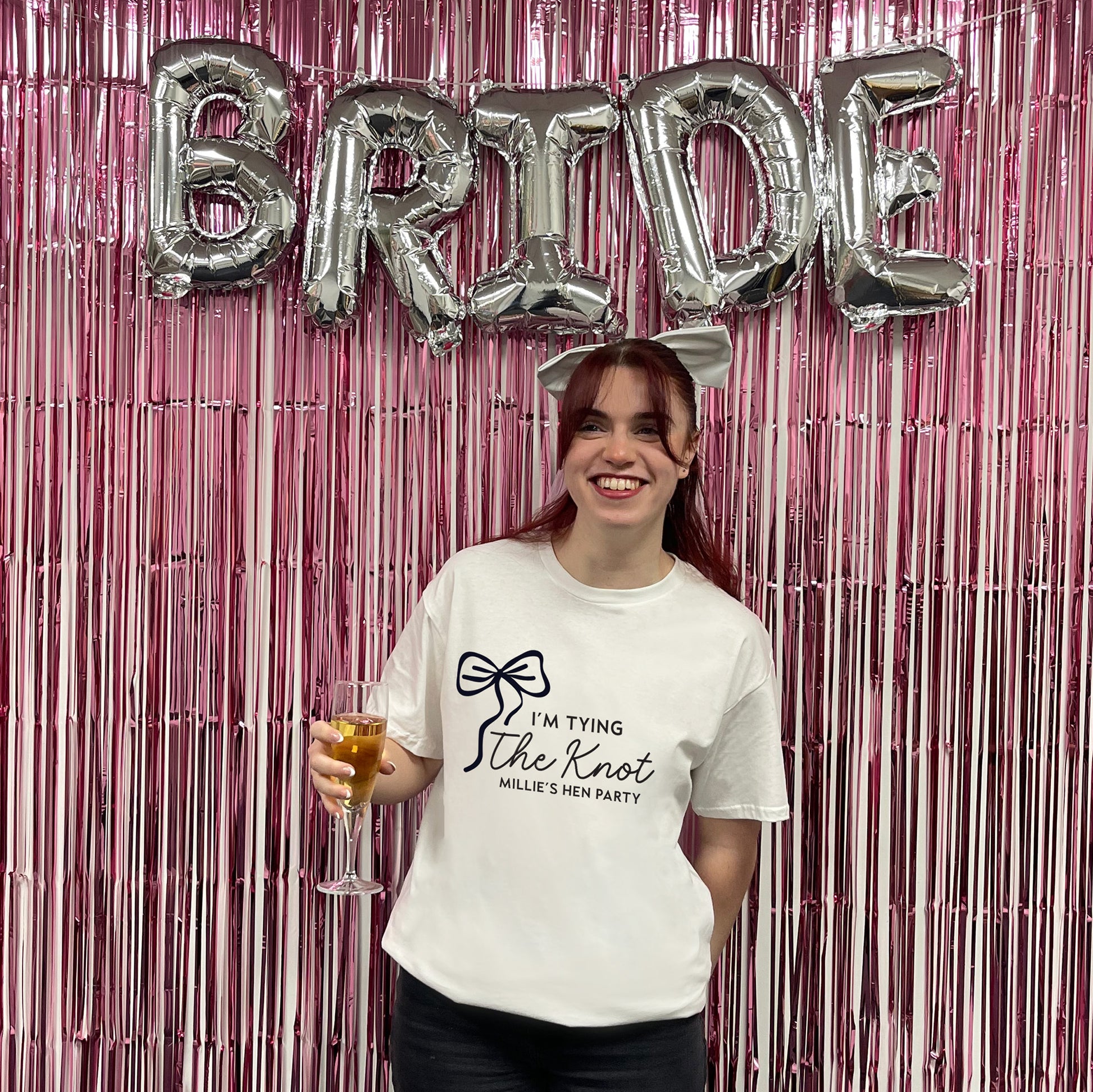Woman holding a glass of champagne with 'Bride' balloons and pink tinsel in the background