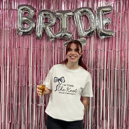 Woman holding a glass of champagne with 'Bride' balloons and pink tinsel in the background