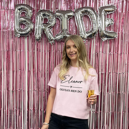 Woman holding a glass of champagne in front of 'BRIDE' balloons and pink tinsel curtain
