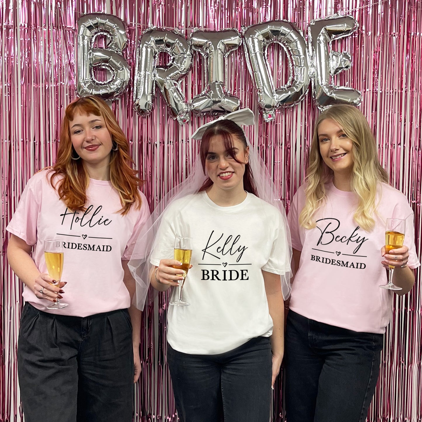 Three women in t-shirts labeled 'Hollie Bridesmaid', 'Kelly Bride', and 'Becky Bridesmaid' with 'BRIDE' balloons in the background.