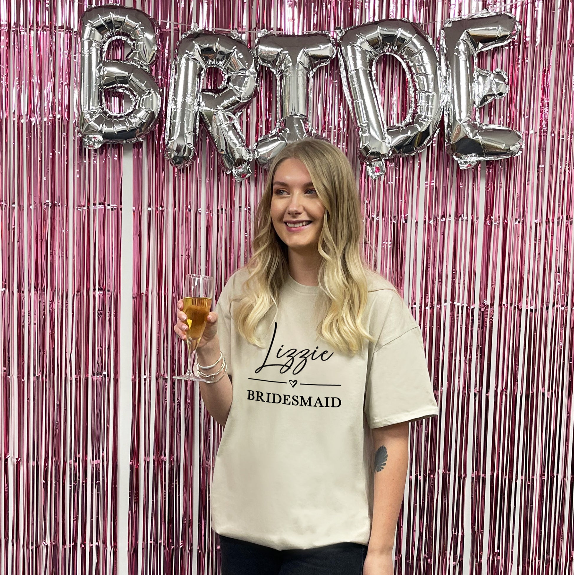 Woman holding a glass of juice with 'Bride' balloons and pink streamers in the background