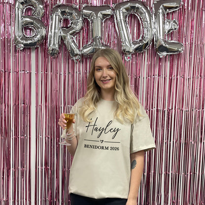 Woman holding a glass of champagne with 'BRIDE' balloons and a pink metallic curtain in the background.