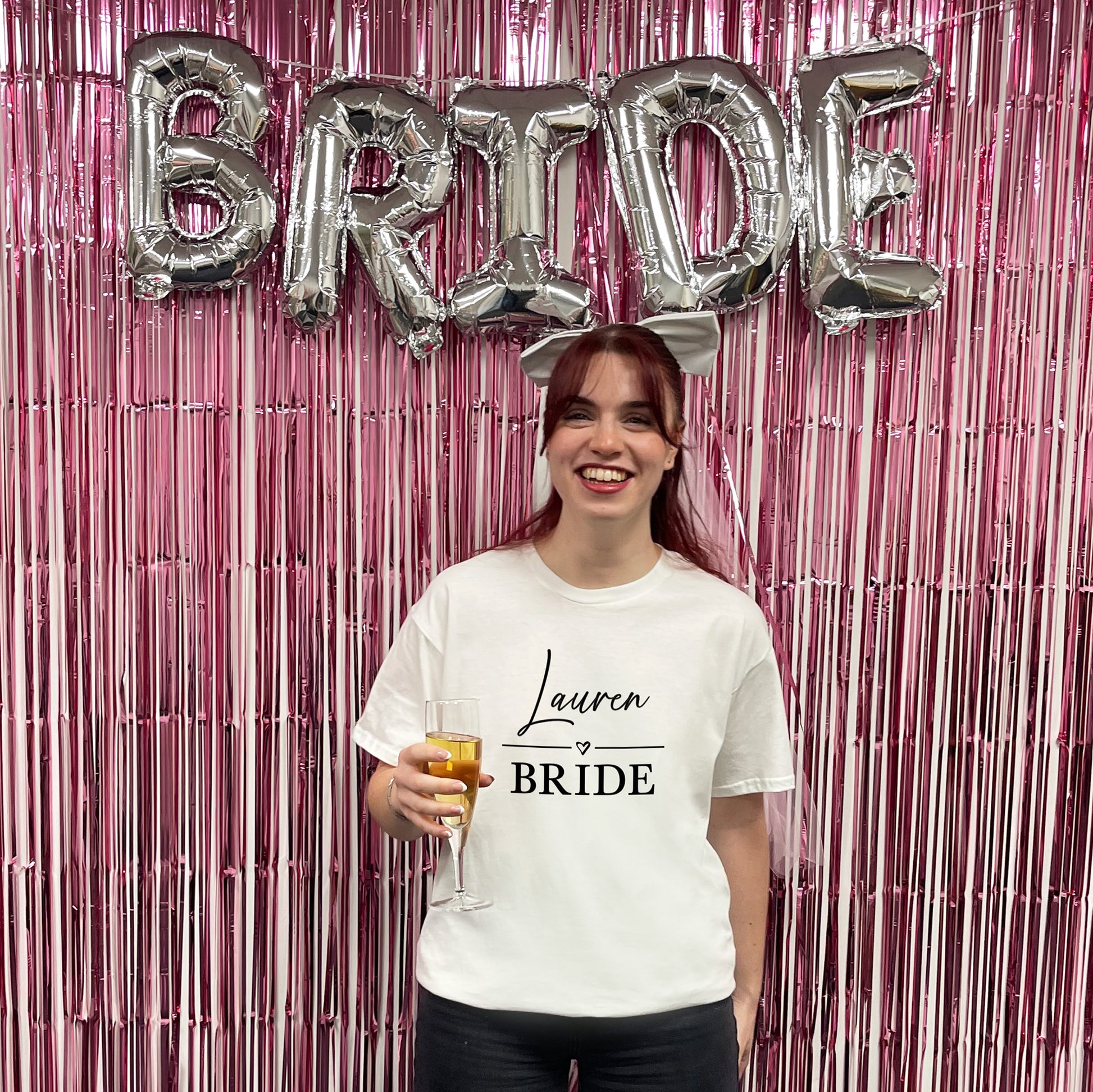 Woman in a 'Lauren Bride' t-shirt with 'BRIDE' balloons and pink fringe curtain