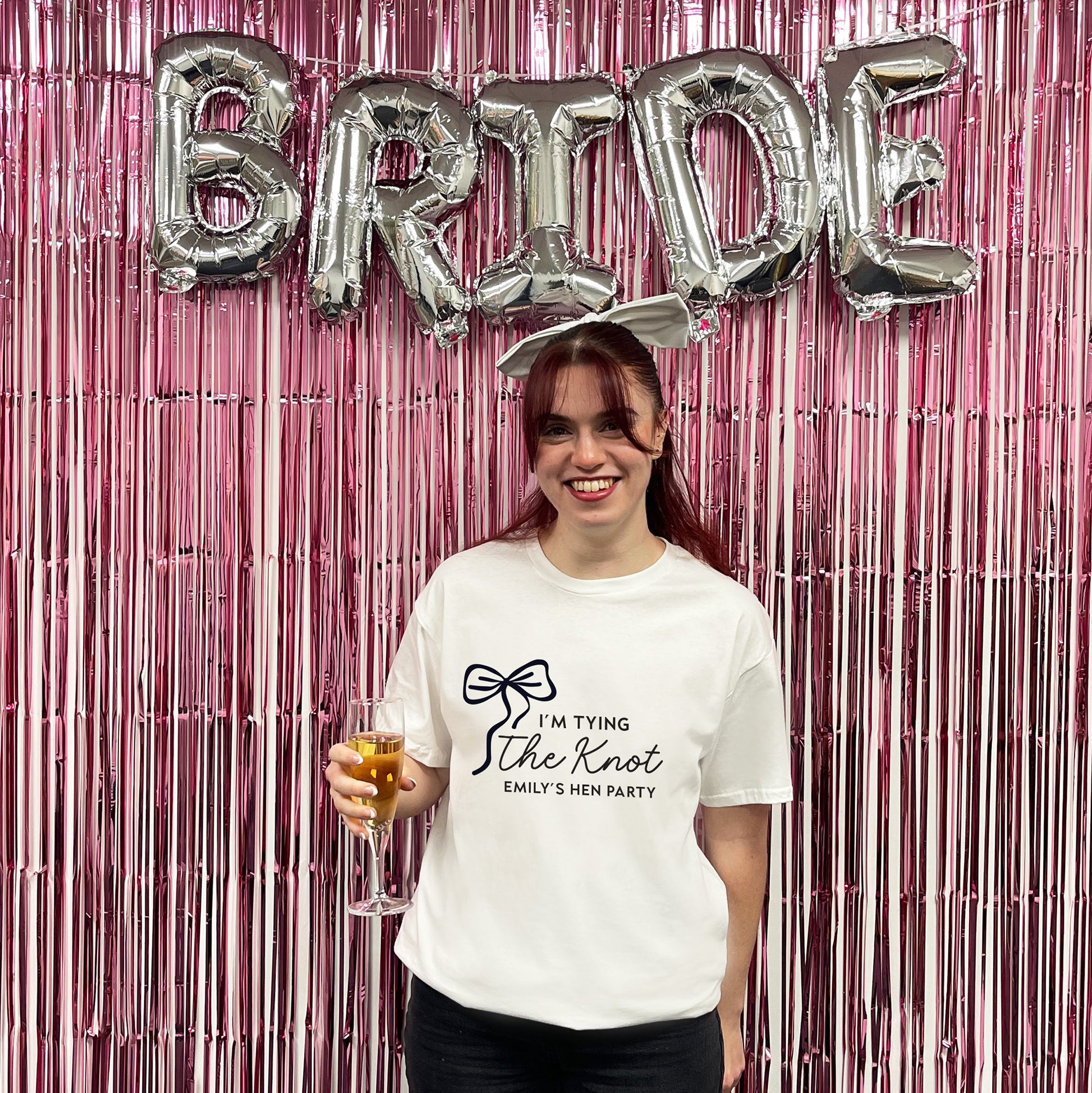 Woman holding a glass of champagne with 'Bride' balloons and pink streamers in the background